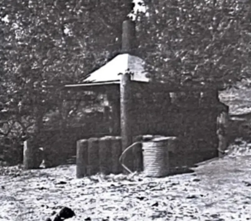 An original historical photo of the BBQ pit that shows it with its roof still on and some other accessories.