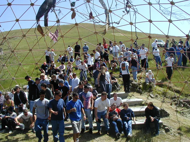 A group of visitors sitting inside the open framework of the Geodesic Dome.